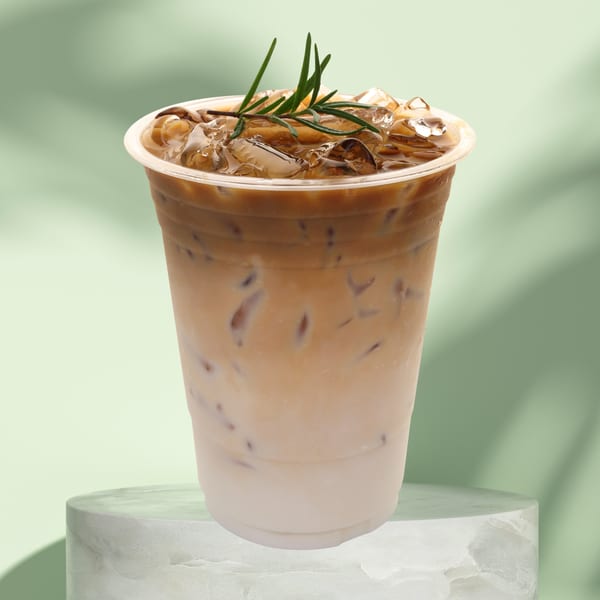 Iced coffee with milk and ice, garnished with rosemary, on a marble pedestal.