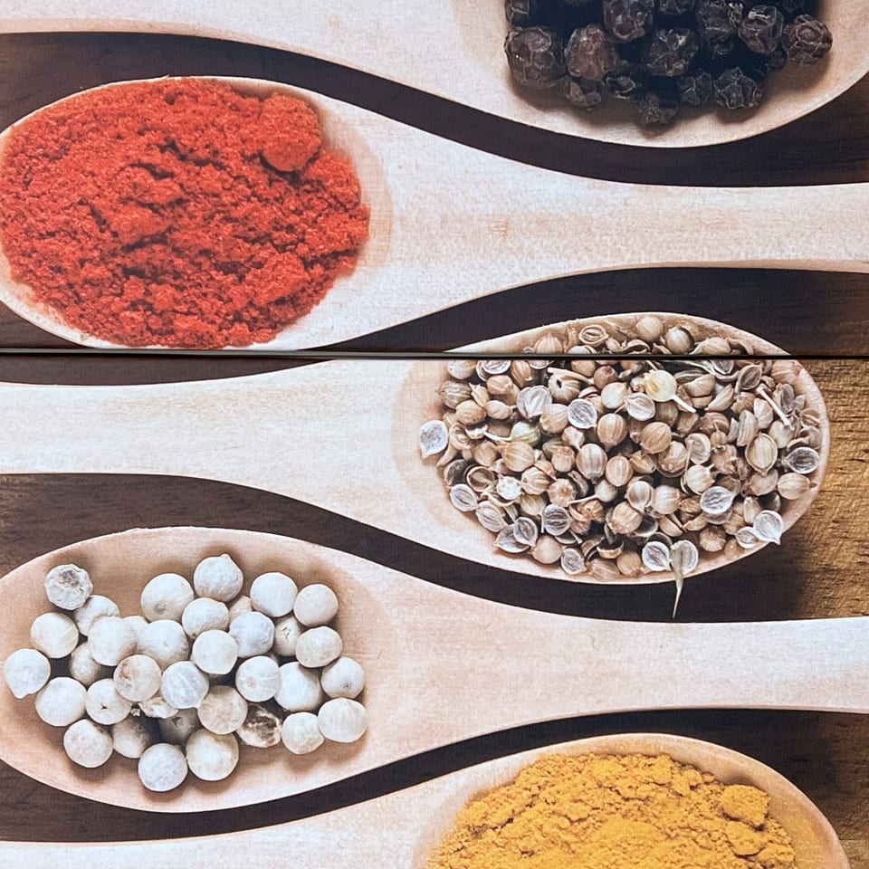 Wooden spoons filled with various Indian spices, including red chili powder, coriander, white peppercorns, and turmeric.