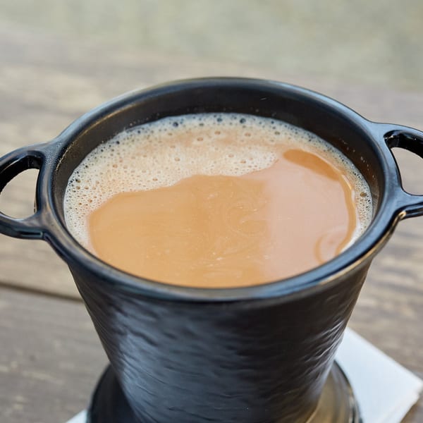 Close-up of a black mug filled with frothy, creamy Indian chai on a wooden table.
