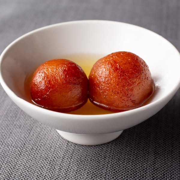 Two gulab jamun, Indian fried dough balls soaked in syrup, in a white bowl.