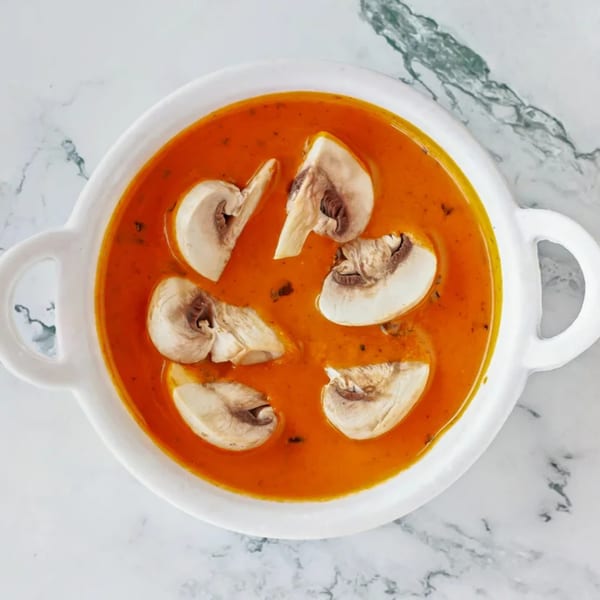 Overhead view of a white bowl filled with orange Indian curry and sliced mushrooms.