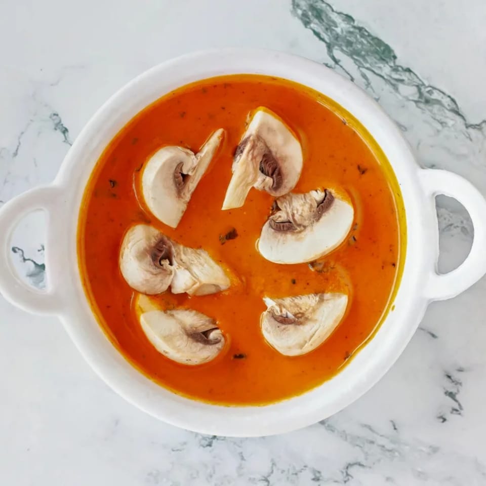 Overhead view of a white bowl filled with orange Indian curry and sliced mushrooms.