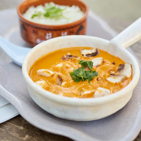 Indian mushroom curry with cilantro in a white bowl, with a side of rice in a brown bowl.